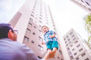 A bright-eyed young boy standing tall in the palm of his father as a skyscraper shoots into the sky in the background